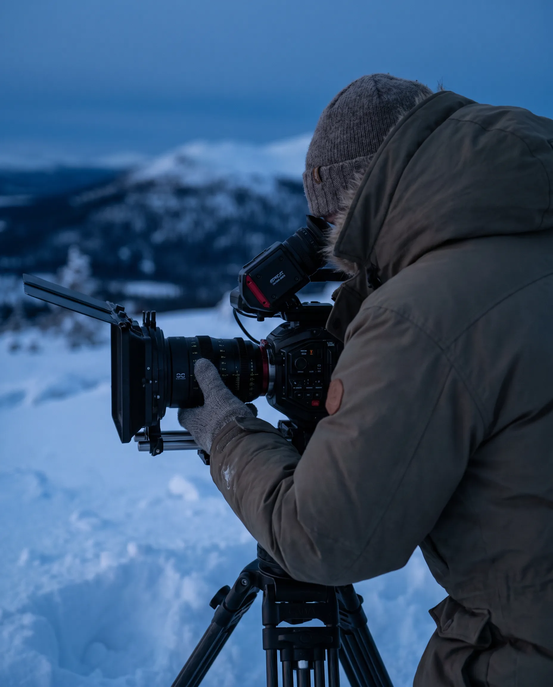 Filmfotograf med kamera på stativ i snö vid blå timmen i fjällen
